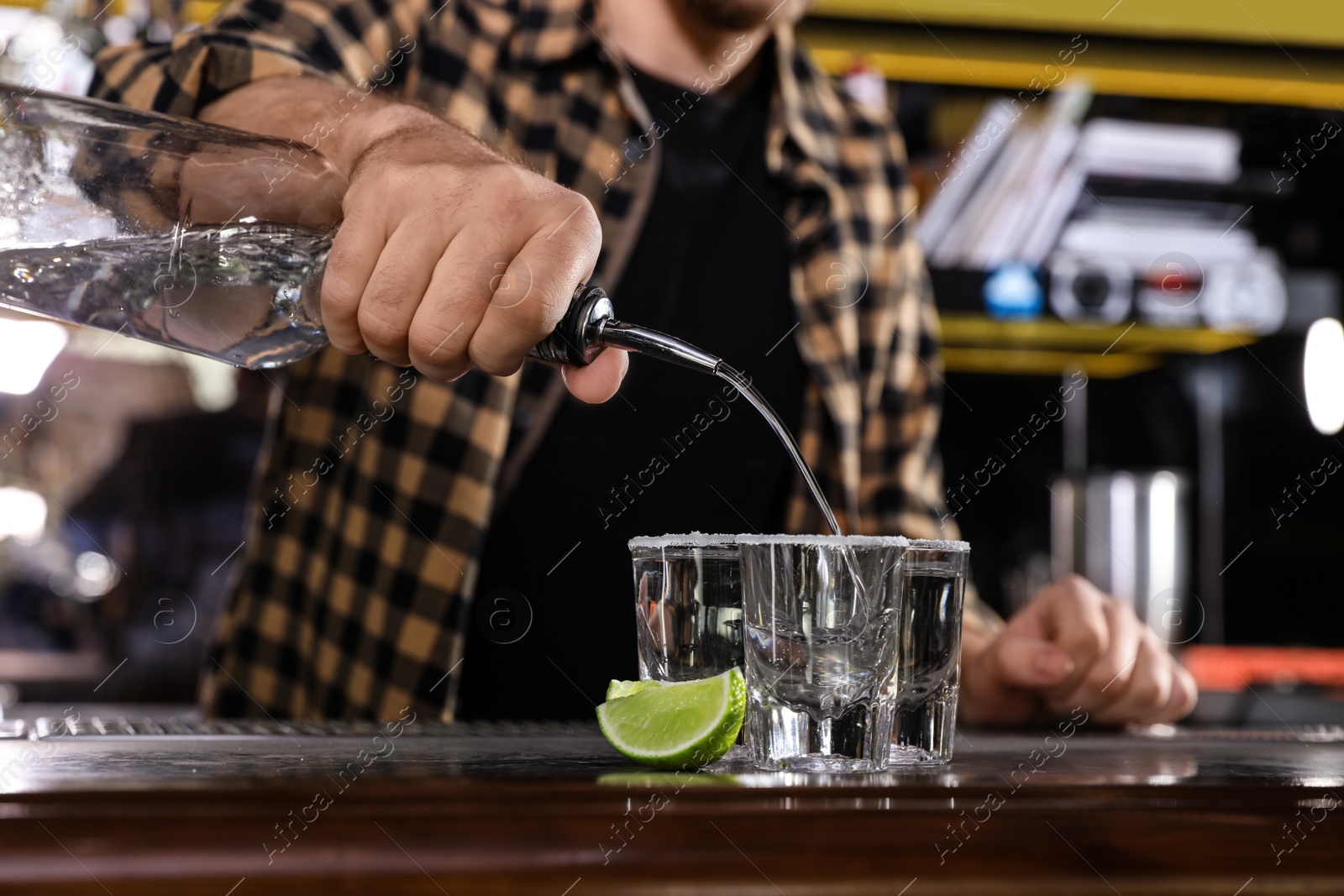 Photo of Bartender pouring Mexican Tequila into shot glasses at bar counter, closeup