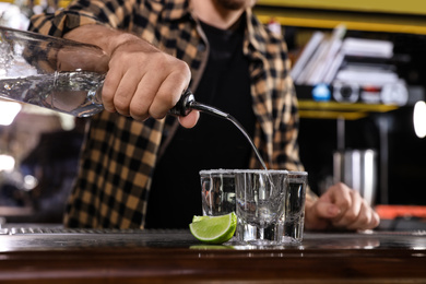 Bartender pouring Mexican Tequila into shot glasses at bar counter, closeup