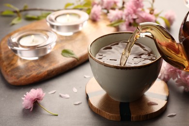 Photo of Traditional ceremony. Pouring brewed tea from teapot into cup on grey table, closeup