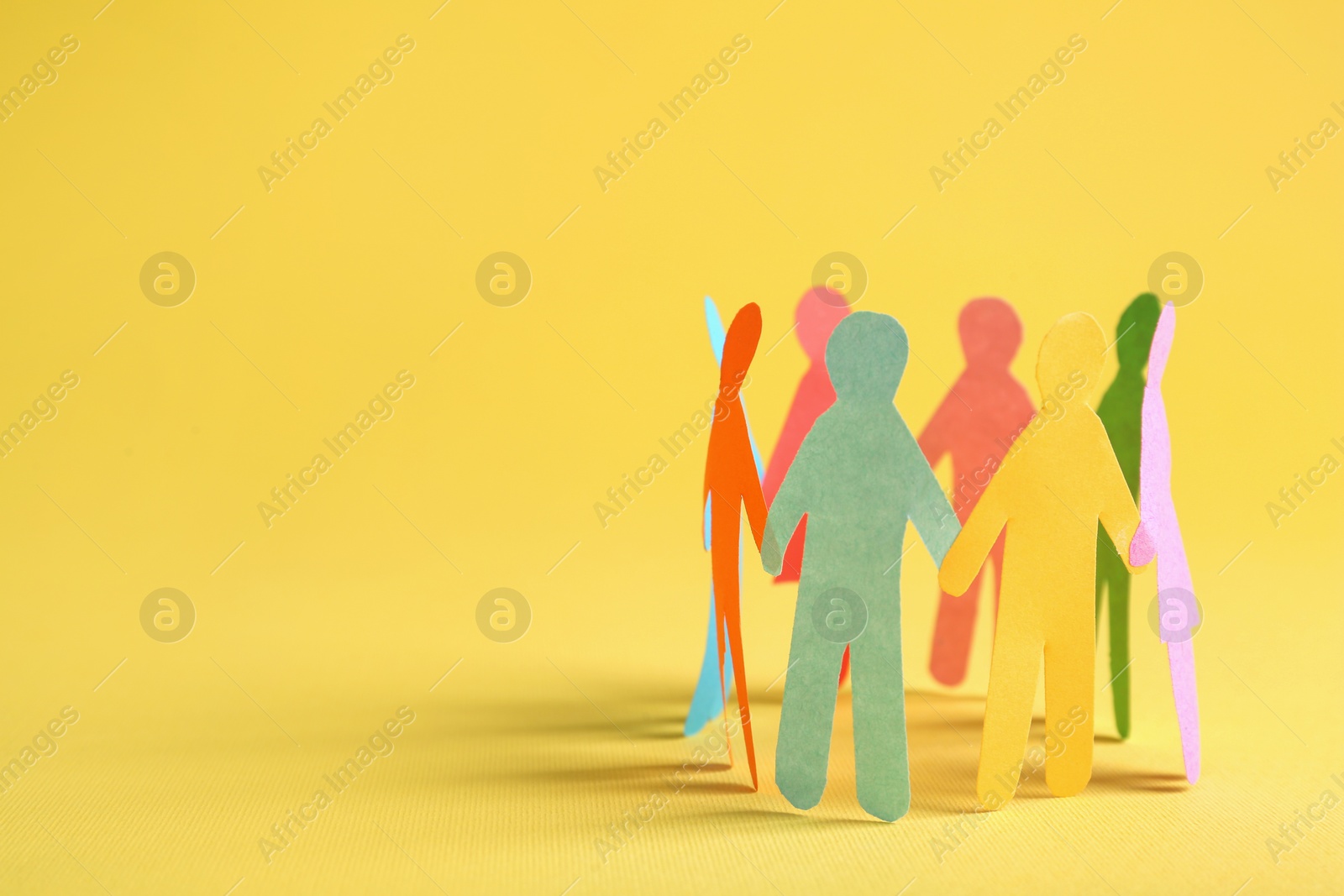 Photo of Many different paper human figures standing in circle on yellow background, space for text. Diversity and inclusion concept