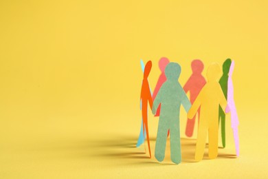 Photo of Many different paper human figures standing in circle on yellow background, space for text. Diversity and inclusion concept