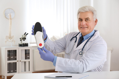 Photo of Senior male orthopedist showing insole in clinic