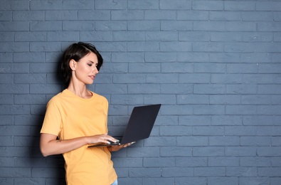 Photo of Young woman with modern laptop on brick wall background