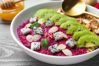 Photo of Bowl of granola with pitahaya, kiwi and almonds on grey wooden table, closeup