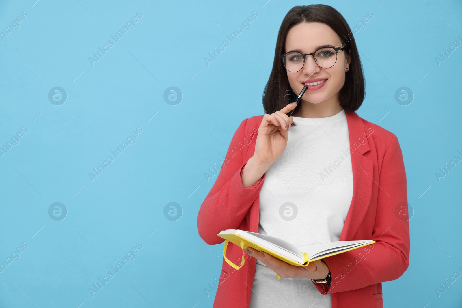 Photo of Happy young intern with notebook and pen on light blue background. Space for text