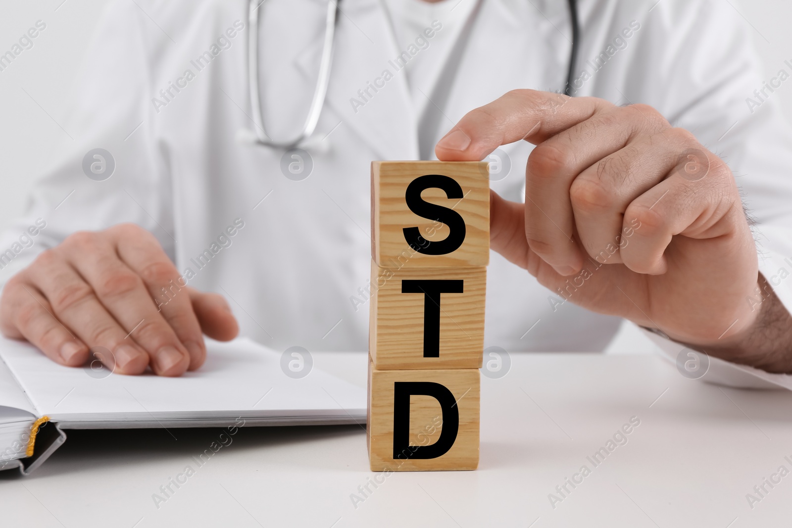 Photo of Doctor and wooden cubes with abbreviation STD at white table, closeup