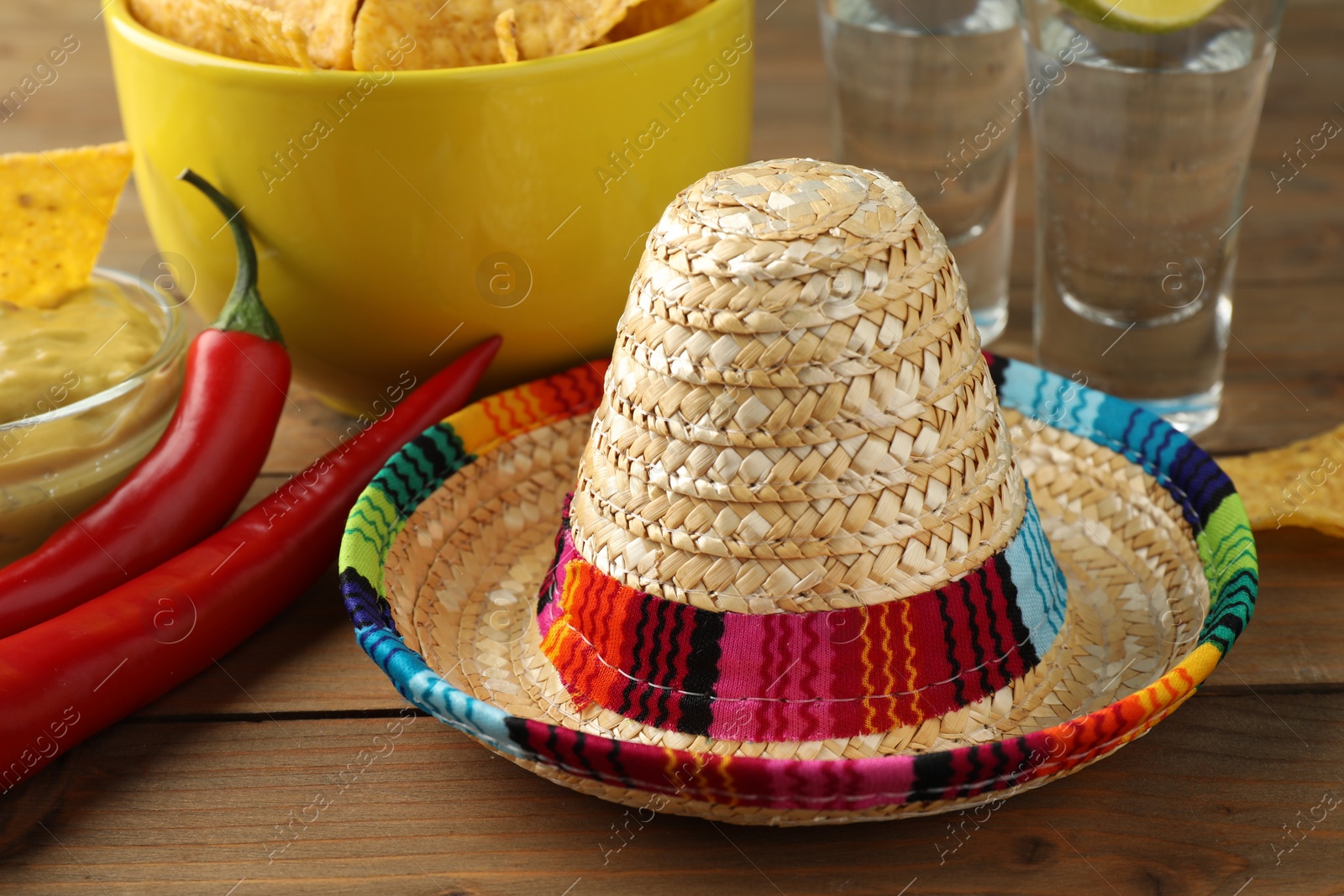 Photo of Mexican sombrero hat and chili peppers on wooden table, closeup