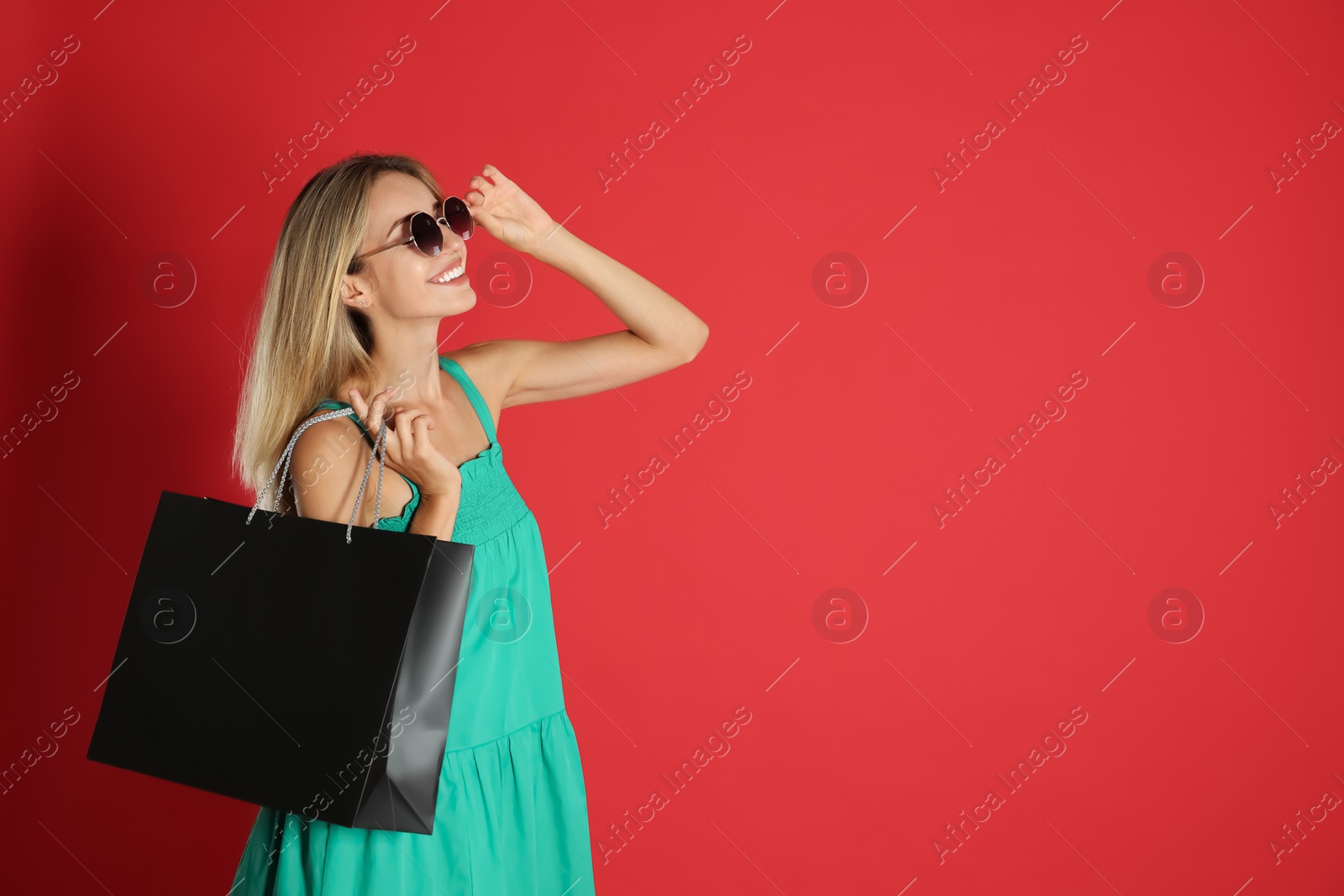 Photo of Happy young woman with shopping bag on red background, space for text. Black Friday Sale