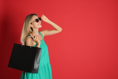 Happy young woman with shopping bag on red background, space for text. Black Friday Sale