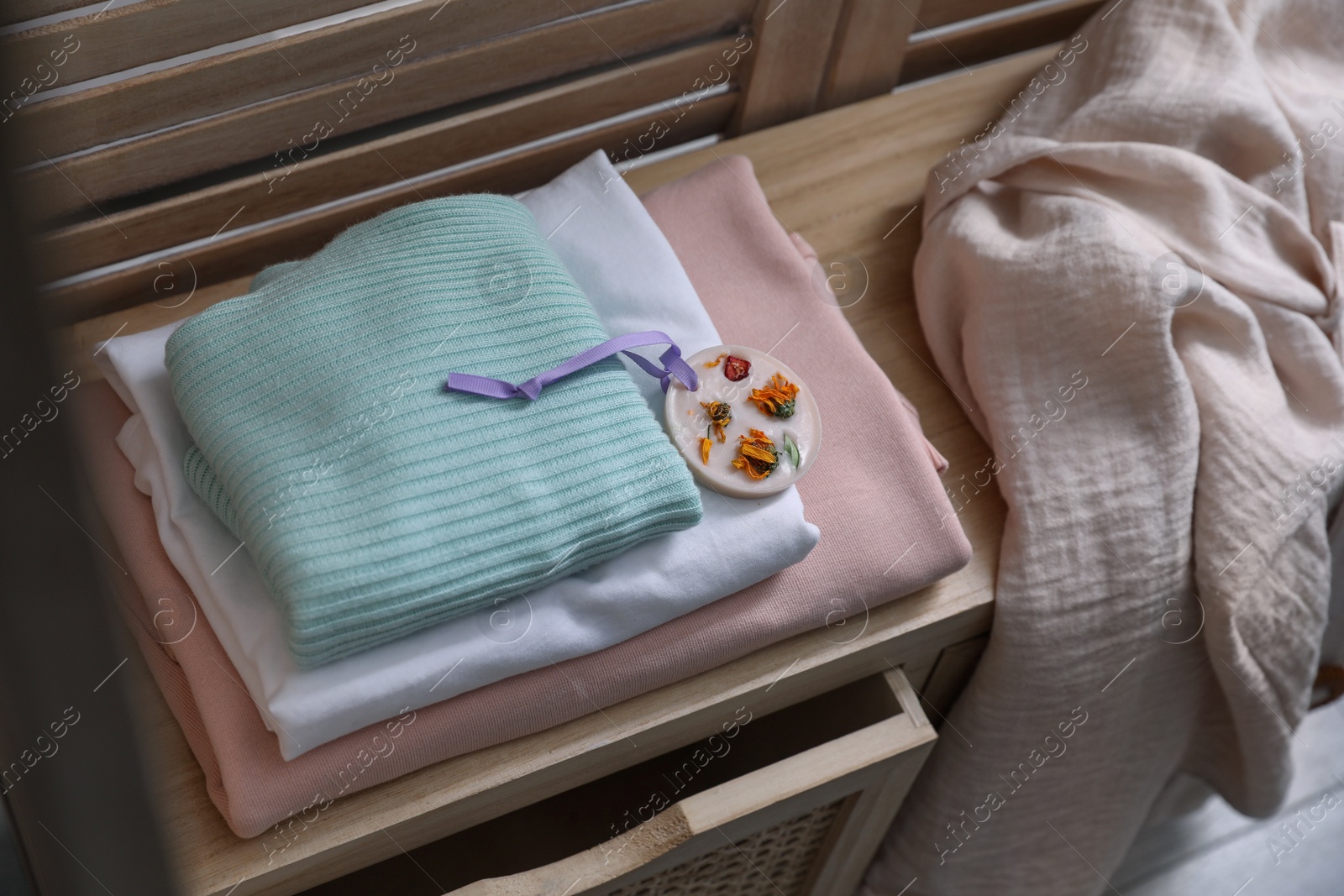 Photo of Beautiful scented wax sachet and stack of clothes on wooden dresser indoors