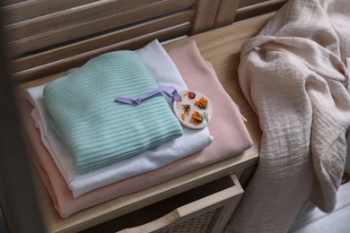 Beautiful scented wax sachet and stack of clothes on wooden dresser indoors