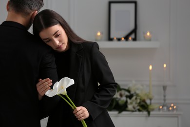 Photo of Sad couple with calla lily flowers mourning indoors, space for text. Funeral ceremony