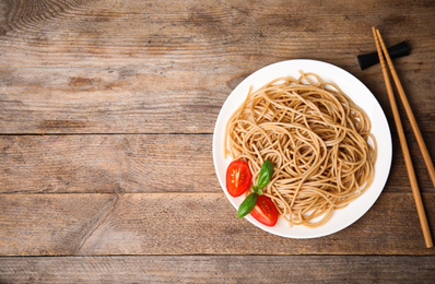 Tasty buckwheat noodles with chopsticks on wooden table, flat lay. Space for text