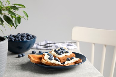 Tasty sandwiches with cream cheese and blueberries on grey table indoors