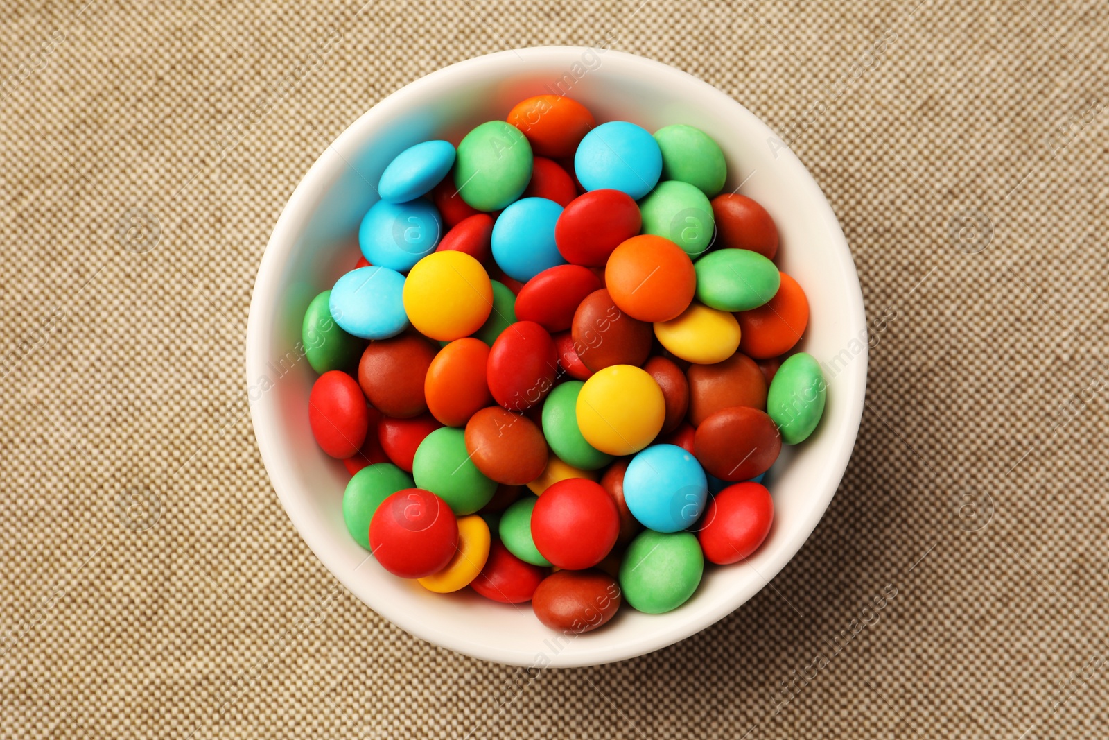 Photo of Bowl with tasty colorful candies on cloth, top view