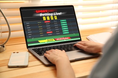 Woman betting on sports using laptop at table, closeup. Bookmaker website on screen