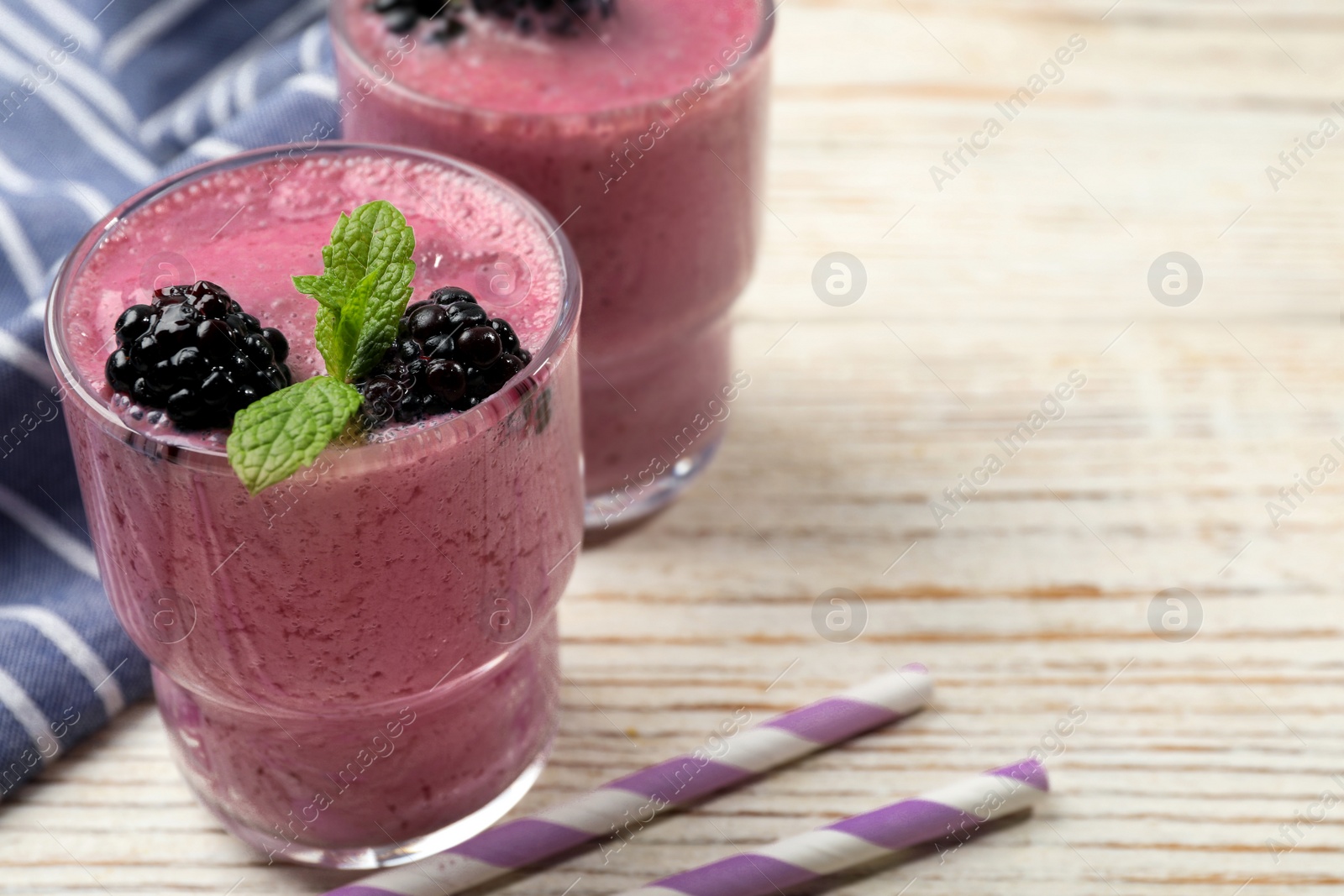 Photo of Glass of blackberry smoothie with mint and berries on light wooden table, closeup. Space for text