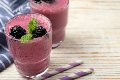 Glass of blackberry smoothie with mint and berries on light wooden table, closeup. Space for text