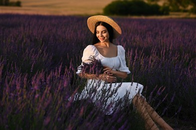 Photo of Beautiful young woman with bouquet sitting in lavender field at sunset