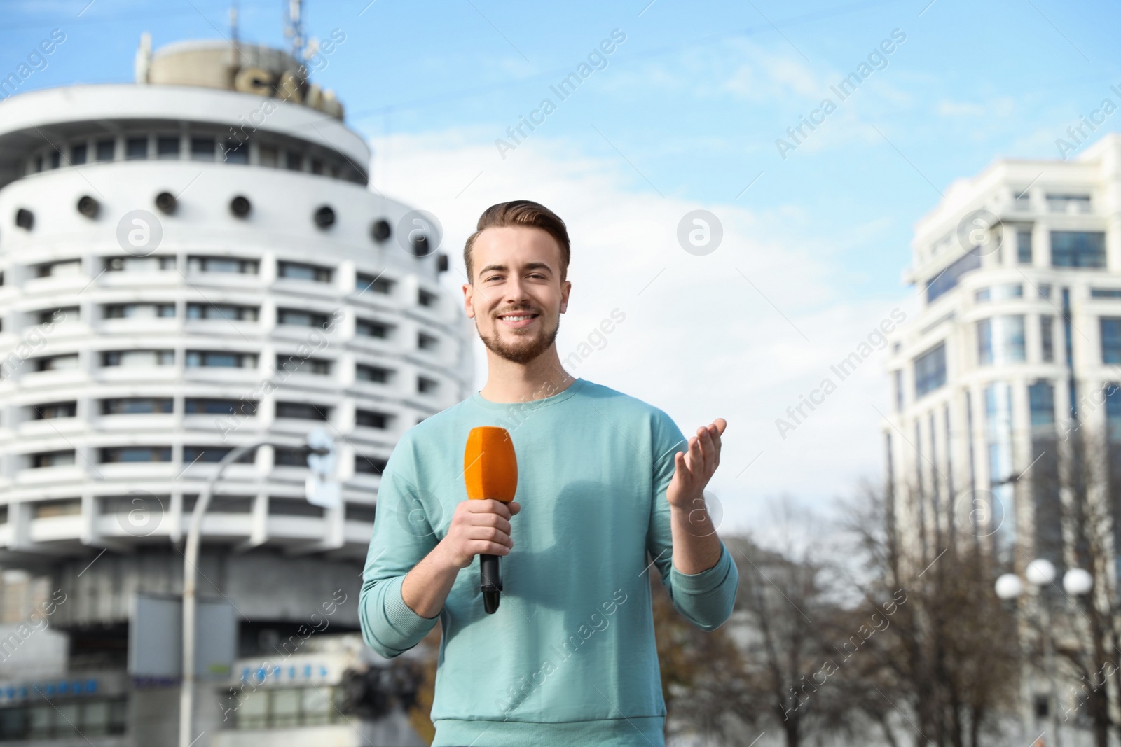 Photo of Young male journalist with microphone working on city street