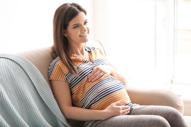 Young pregnant woman sitting on couch in living room