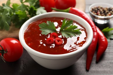 Photo of Spicy chili sauce with parsley on wooden table, closeup