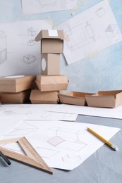 Photo of Creating packaging design. Drawings, boxes and stationery on blue textured table, closeup