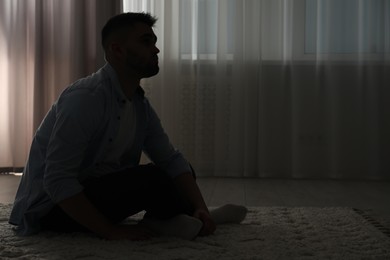 Photo of Silhouette of sad man in dark room. Space for text