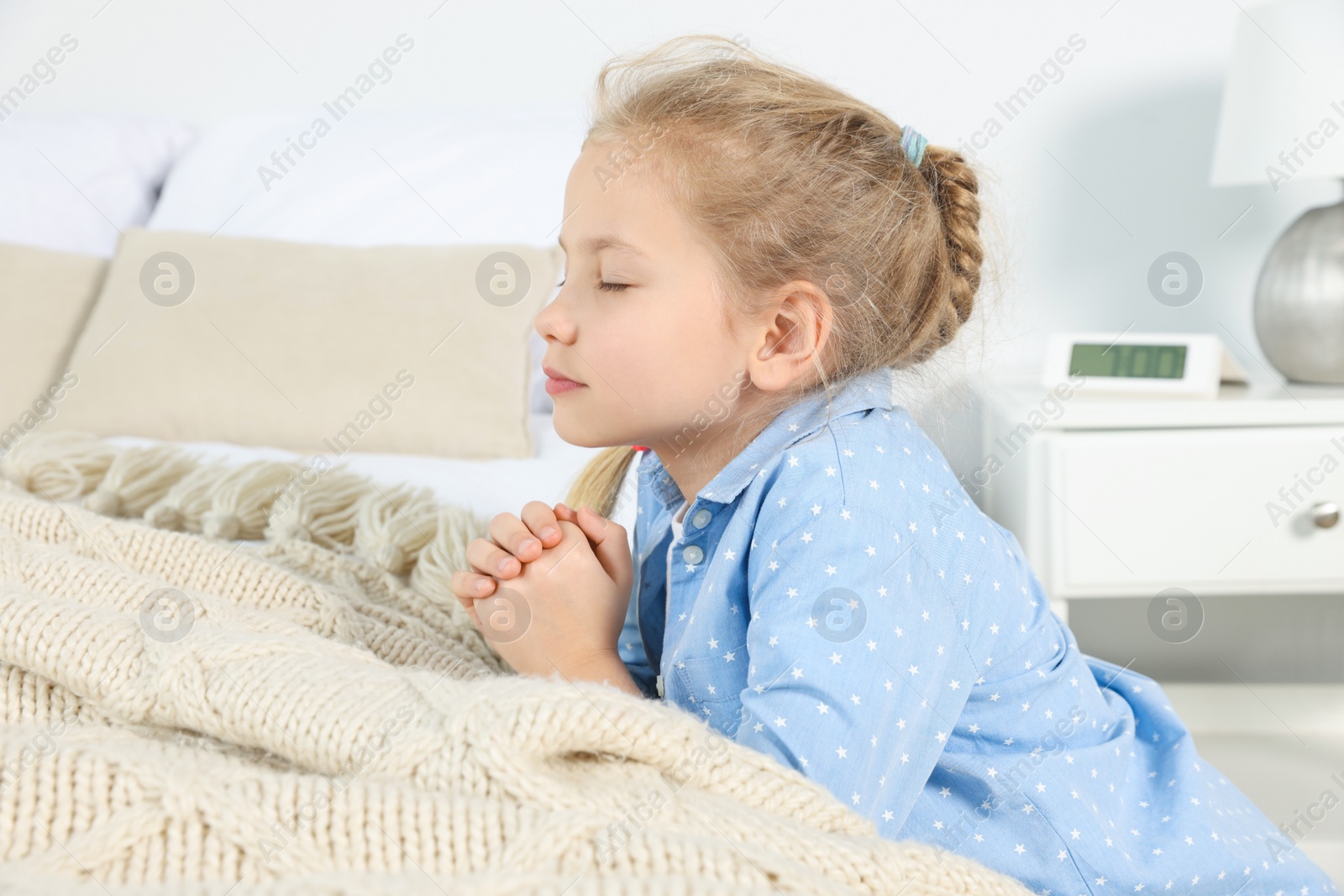 Photo of Girl with clasped hands praying near bed at home