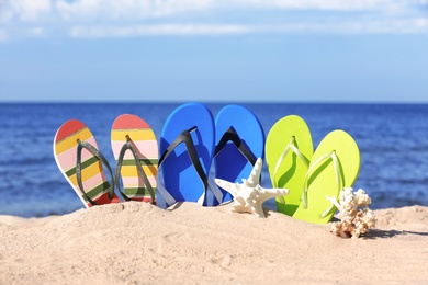 Photo of Composition with bright flip flops on sand near sea in summer. Beach accessories