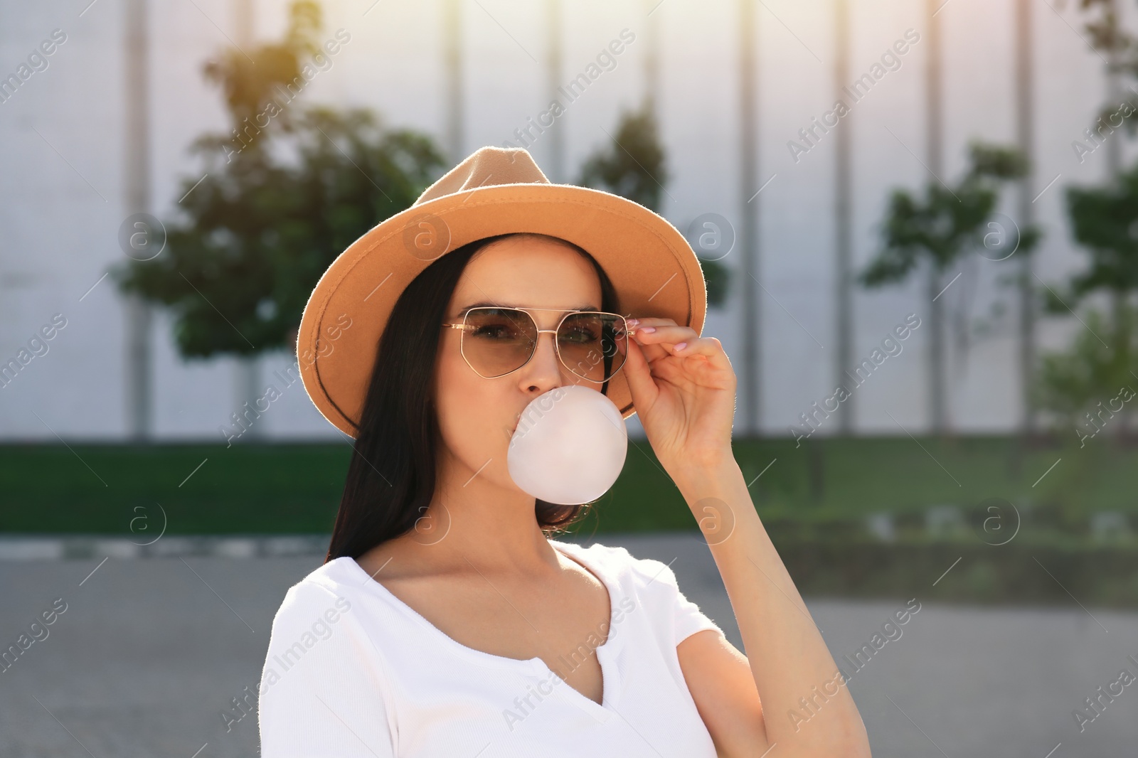 Photo of Beautiful woman in stylish sunglasses blowing gum outdoors on sunny day