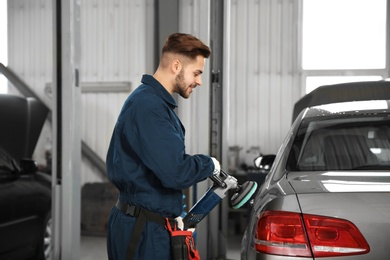 Technician polishing car body with tool at automobile repair shop