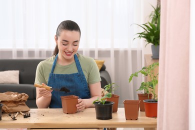 Photo of Happy woman planting seedling into pot at wooden table in room