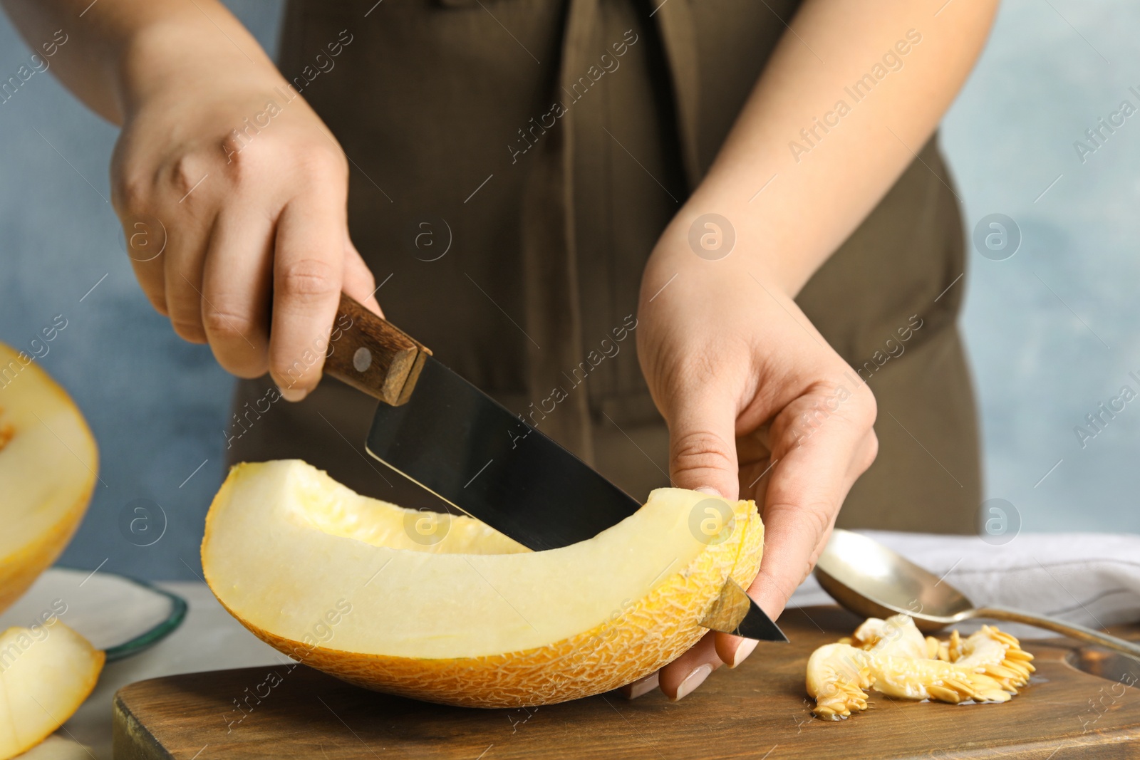 Photo of Young woman cutting ripe melon on board at table, closeup