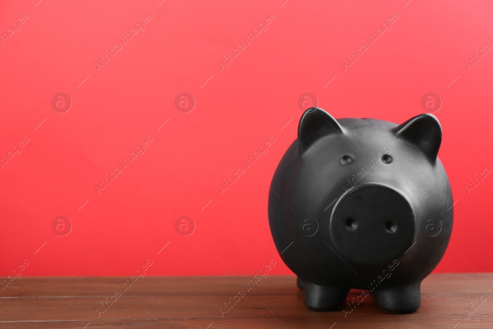 Photo of Black piggy bank on wooden table against red background. Space for text