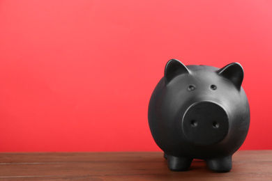Photo of Black piggy bank on wooden table against red background. Space for text