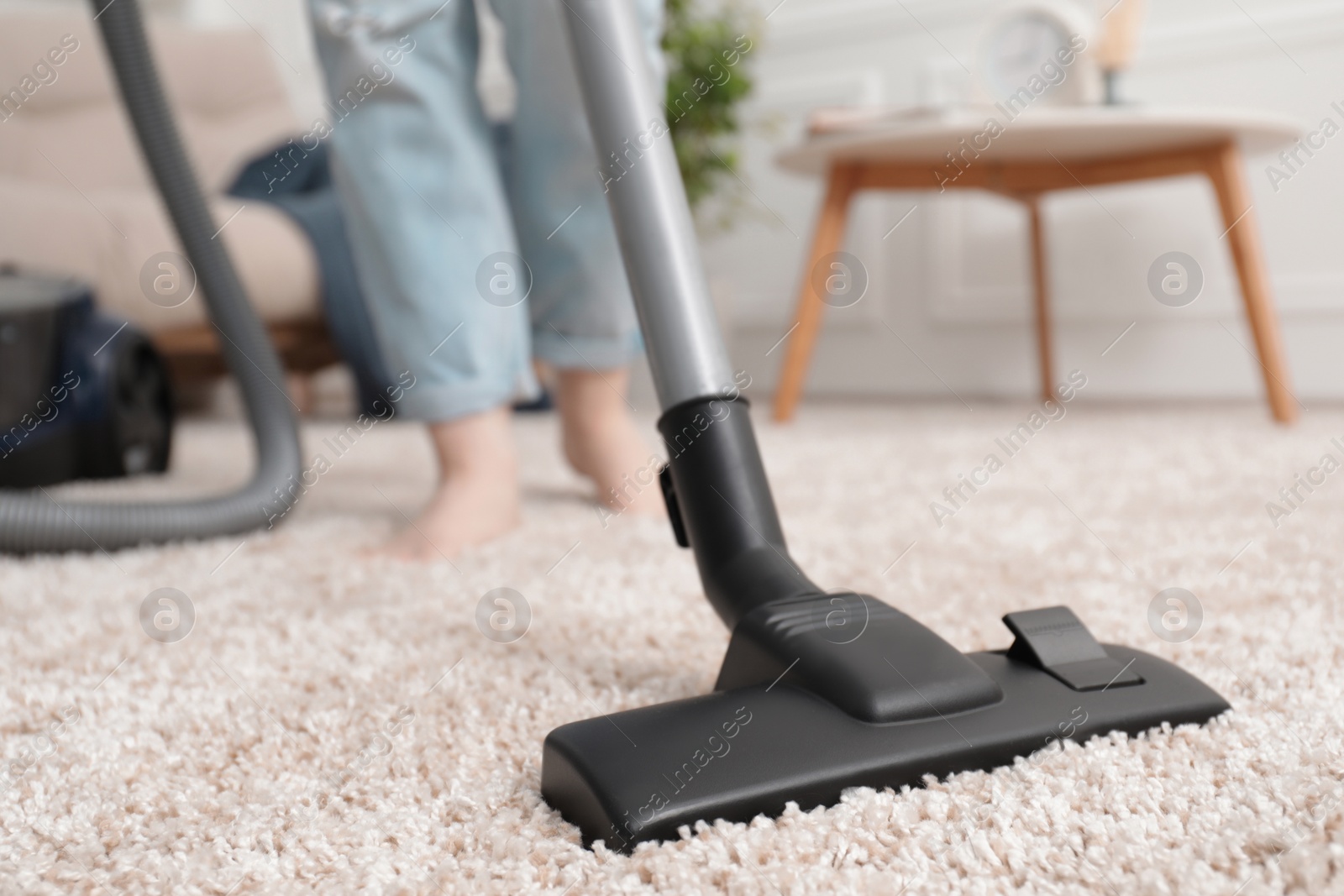 Photo of Woman cleaning carpet with vacuum cleaner at home, closeup