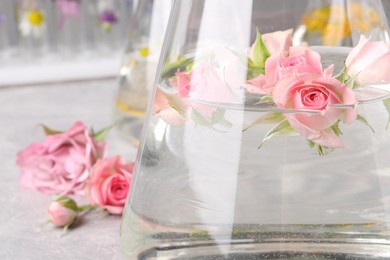 Photo of Flask with rose flowers on table, closeup. Essential oil extraction