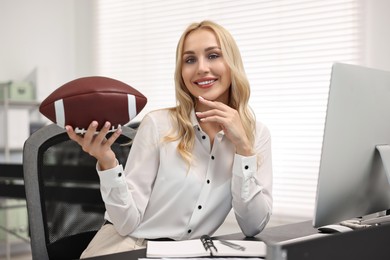 Happy woman with american football ball at table in office