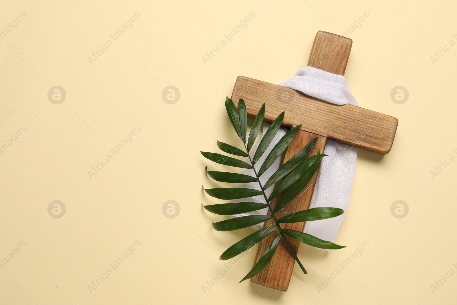 Photo of Wooden cross, white cloth and palm leaf on beige background, top view with space for text. Easter attributes