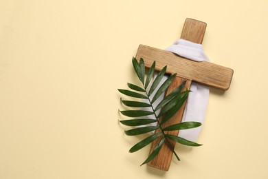 Wooden cross, white cloth and palm leaf on beige background, top view with space for text. Easter attributes