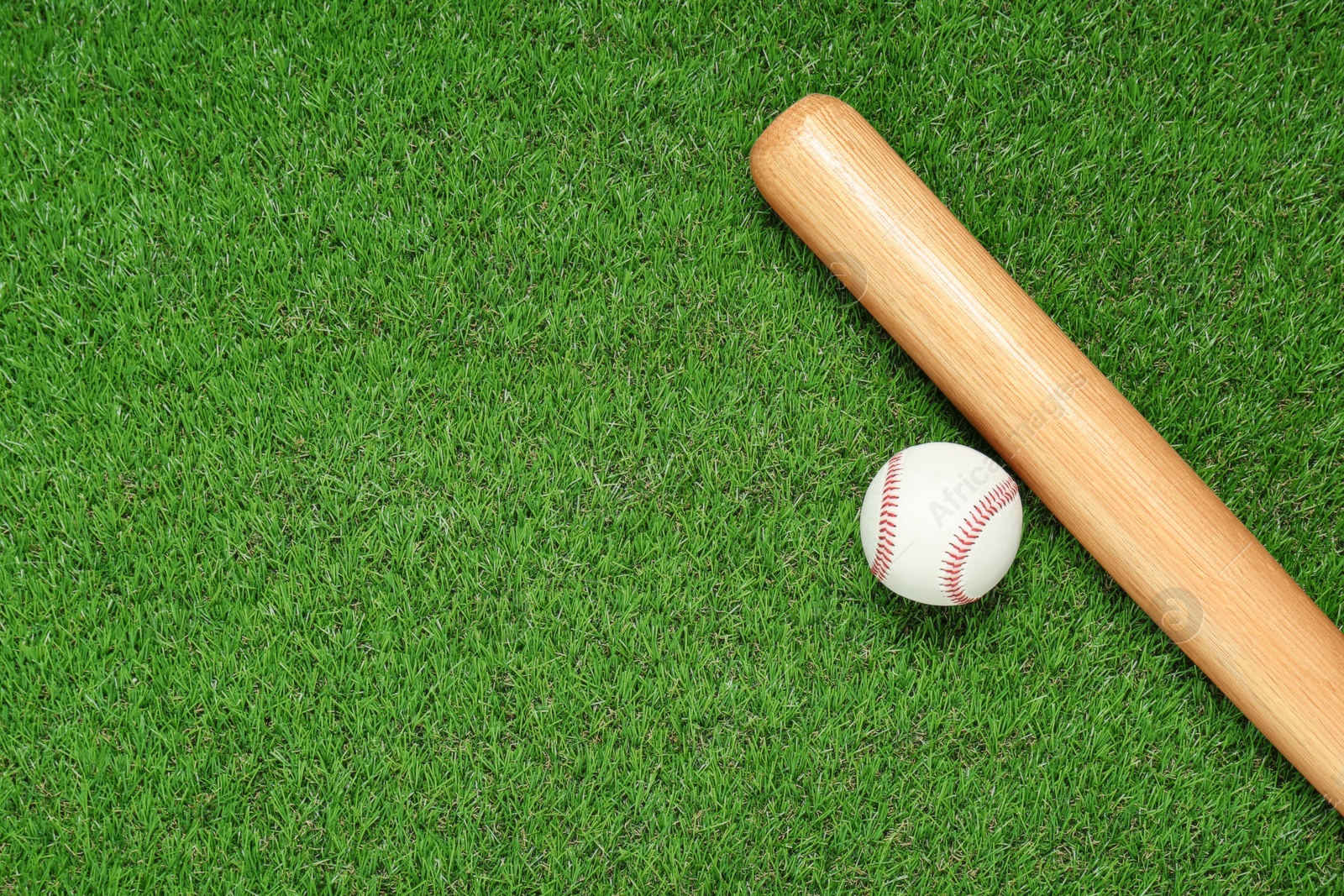 Photo of Wooden baseball bat and ball on green grass, flat lay. Space for text