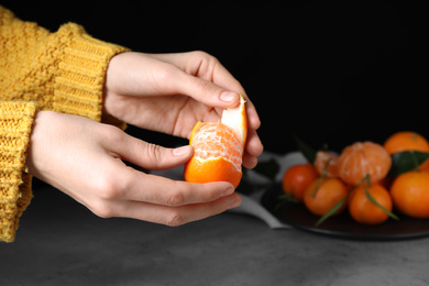 Photo of Woman peeling fresh ripe tangerine on black background, closeup