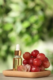 Fresh grapes and bottle of essential oil on wooden table