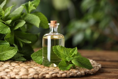 Photo of Bottle of mint essential oil and green leaves on wooden table, closeup