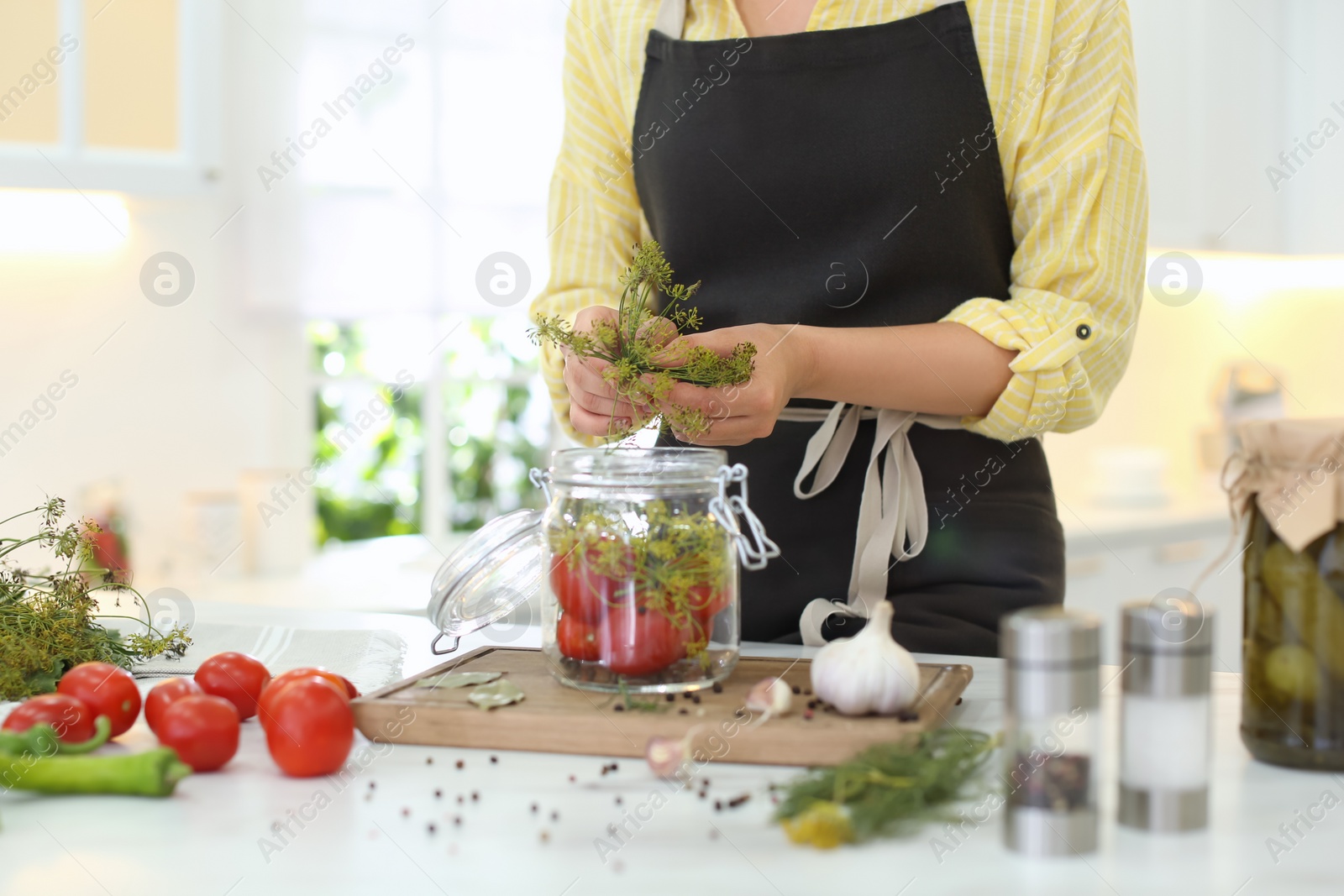 Photo of Woman putting dill into pickling jar at table in kitchen, closeup