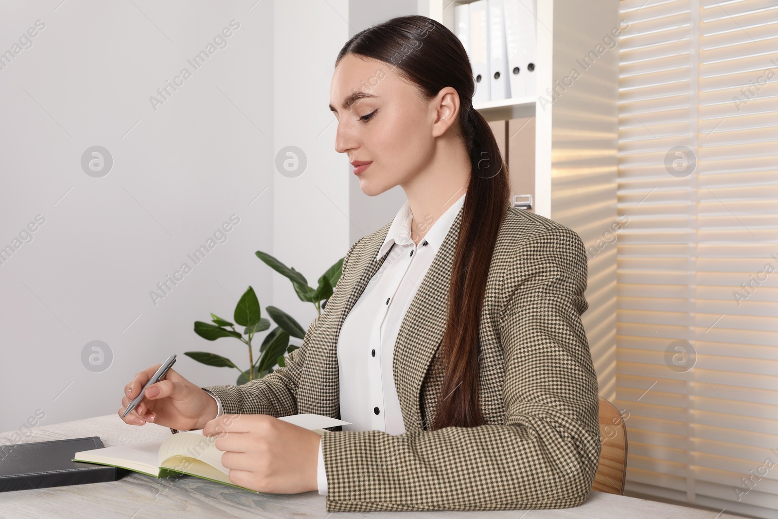 Photo of Woman taking notes at light wooden table in office