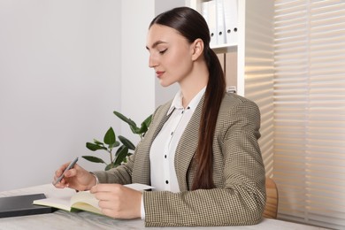 Woman taking notes at light wooden table in office