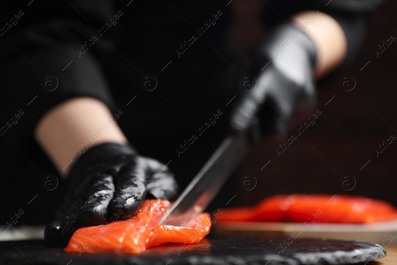 Photo of Chef in gloves cutting salmon for sushi at table, closeup