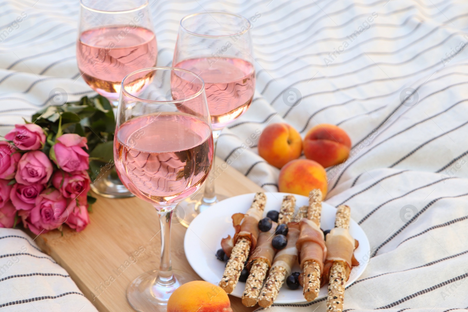 Photo of Glasses of delicious rose wine, flowers and food on white picnic blanket